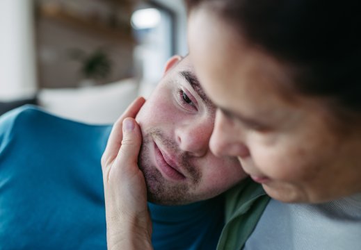 Ung mann legger hode på skulder til omsorgsperson, hun holder en hånd på kinnet hans
