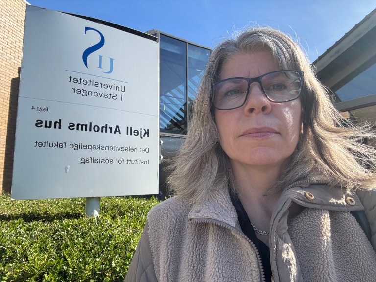 Kvinne foran et skilt som viser Universitetet i Stavanger.