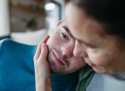 Ung mann legger hode på skulder til omsorgsperson, hun holder en hånd på kinnet hans