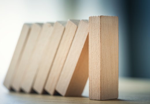 Dominobrikker i tre. Brikkene faller mot den siste, som er stående. Blå bakgrunn. 