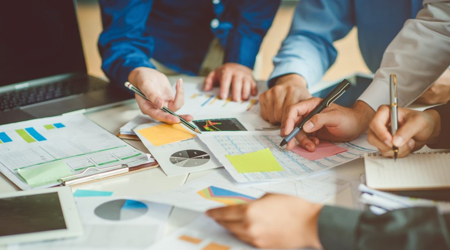 Mennesker som team jobbe sammen, hender holder blyanter og peker på papir som ligger på bordet, utsnittet er av armer og hender.