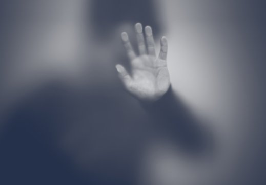 Silhuett av mann som holder en hånd mot frostet glassvegg. Foto svart hvitt.