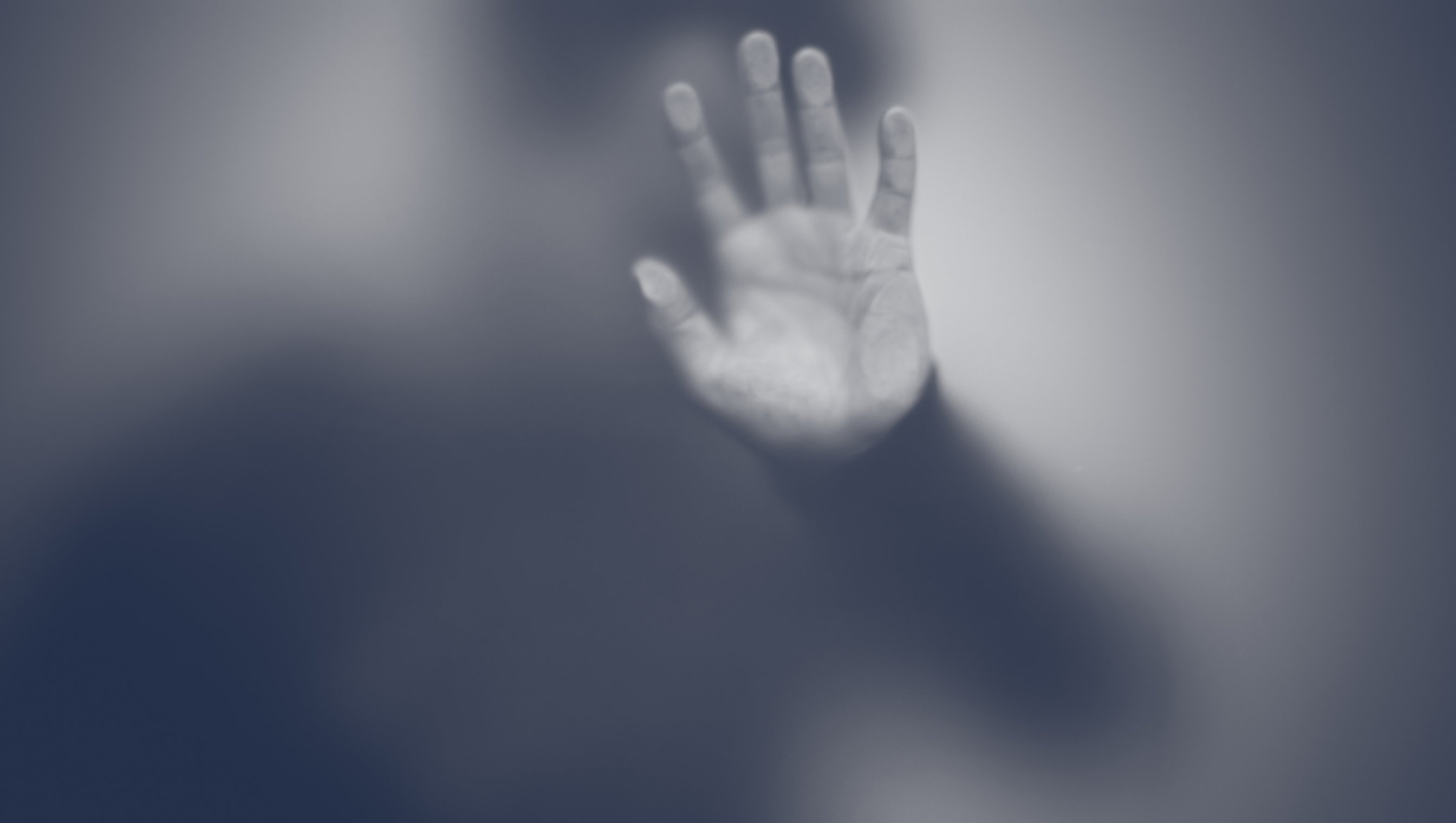 Silhuett av mann som holder en hånd mot frostet glassvegg. Foto svart hvitt.