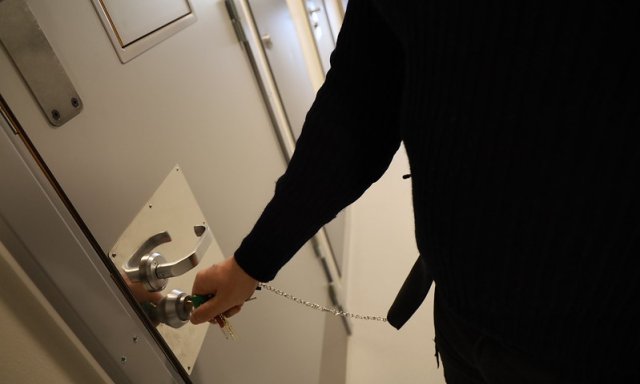 Fengselsbetjent låser en fengselsdør med nøkkel.
