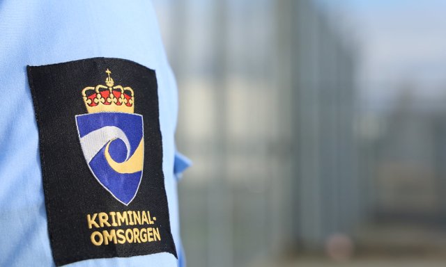 Fengselsbetjent arm blå uniform med logo som viser Kriminalomsorgen