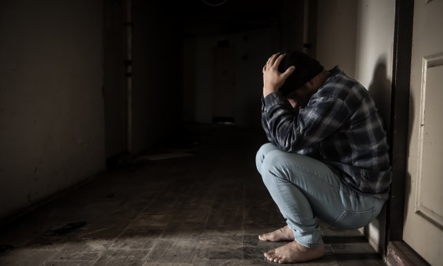 Mann sitter på huk, lener seg til vegg og holder hodet i hendene