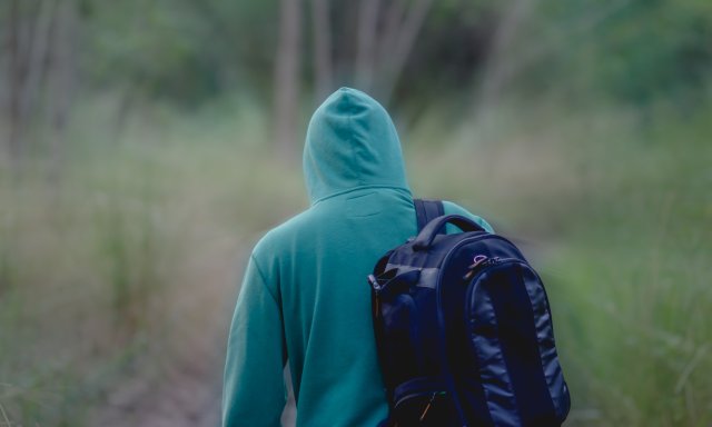 Mann med hettegenser, hette over hodet, med ryggsekk og rygg mot kamera, går ute i naturen