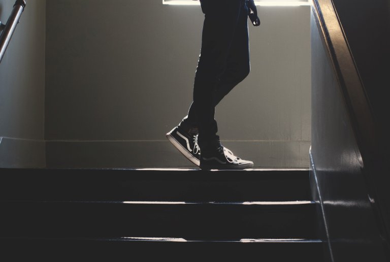 Person i fritidssko på vei opp en mørk trappeoppgang, står midtveis med lysskinn fra vindu. Foto: Unsplash