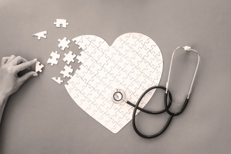 Hjerteformet puzzel, som mangler biter oppe til venstre. Hånd pusler sammen hjertet. Stetoskop ligger over hjertepuzzlet.