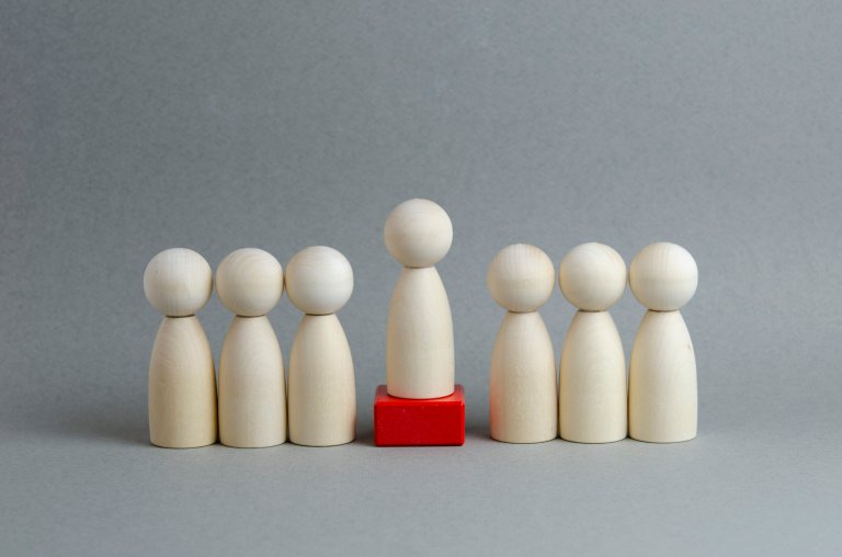 Trefigurer som illusterer et team og leder, leder er plassert på en rød kloss_grå bakgrunn