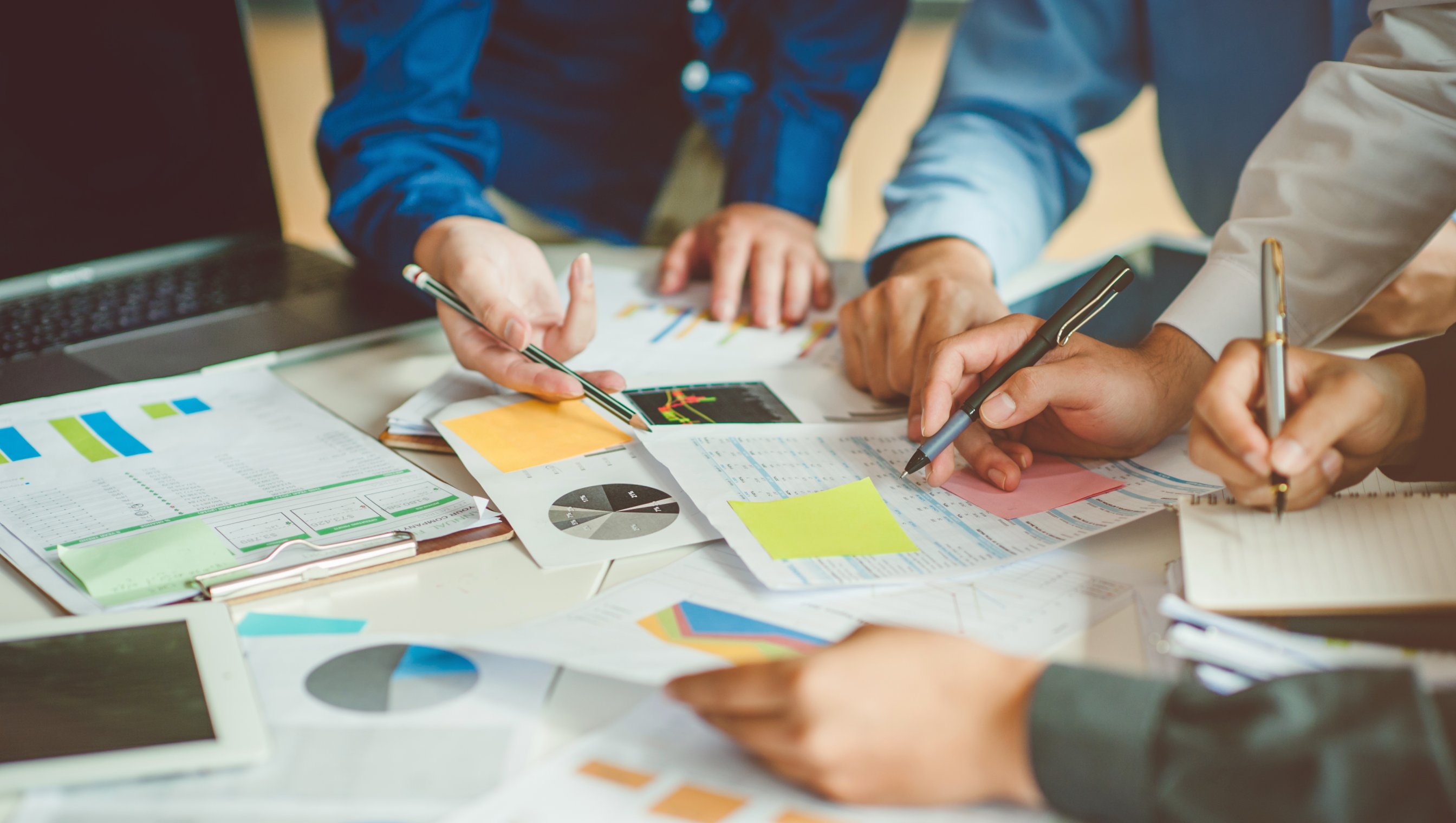 Mennesker som team jobbe sammen, hender holder blyanter og peker på papir som ligger på bordet, utsnittet er av armer og hender.