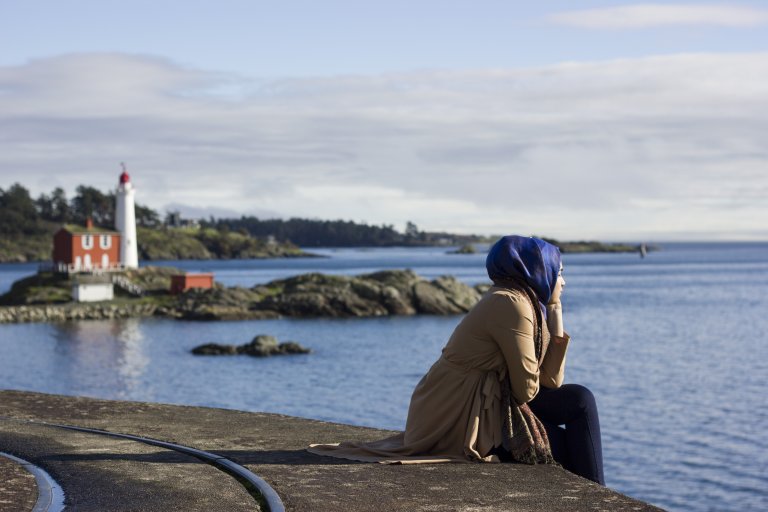 Kvinne sitter på kaia og ser tenkende ut over havet.