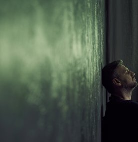 Mann lener hodet inntil en vegg