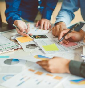 Mennesker som team jobbe sammen, hender holder blyanter og peker på papir som ligger på bordet, utsnittet er av armer og hender.